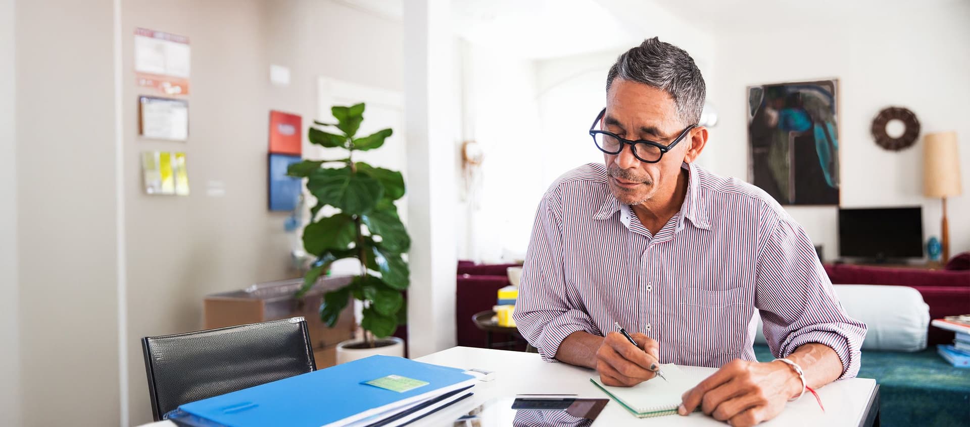 Ein Mann sitzt in seinem Wohnzimmer am Tisch und erledigt Papierkram.