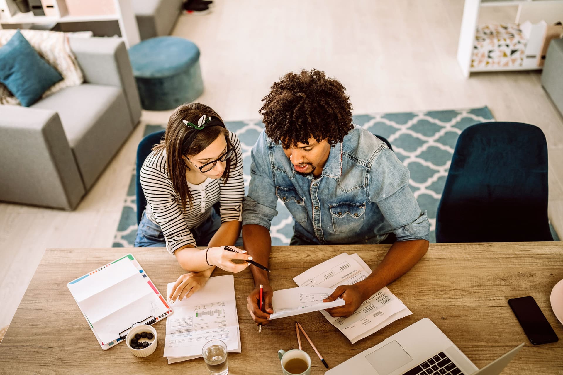 Blick von oben auf ein junges Paar, das an einem Tisch gemeinsam Unterlagen bespricht.
