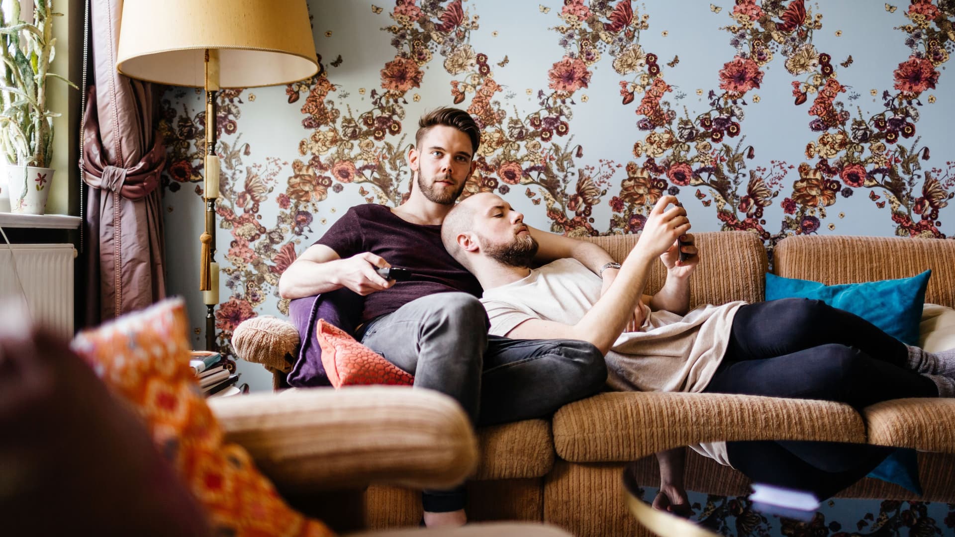 Ein männliches Paar sitzt entspannt auf der Couch und schaut Fernsehen.